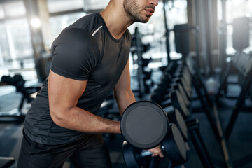 Close-up of athletic man exercising with dumbbell in gym. Focus on muscular arm and intense...