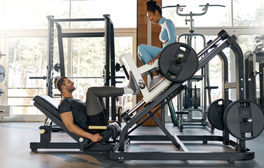 Playful moment at the gym as a man performs leg press exercise while a smiling woman sits on the...