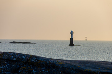 Two solitary lighthouses stand in calm waters under soft evening light. A serene seascape with...