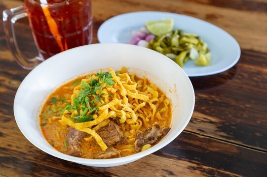 Curried noodle soup (Khao soi) with beef and spicy coconut milk on wood table. Thai food cuisine northern style in Chiang Mai. - Powered by Adobe
