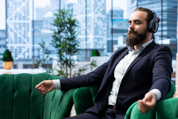 Male leader relaxes during a work break using sound healing to reduce stress. CEO with a calm and...