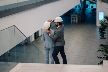 Architect placing hardhat on female colleague in modern office building
