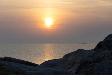 Soft sunset over the sea with rocky foreground. A calm coastal scene in warm pastel tones from the Nordic archipelago.