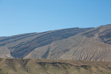 Layered rock formations and arid mountain slopes in Hormozgan, Iran, revealing striking geological textures beneath a clear blue sky.