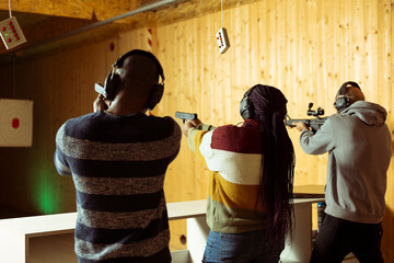 Friends having fun in shooting gallery using guns to hit targets with ammo. Mates entertained by...