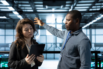 Teamworking admins in data center automating routine maintenance tasks with tablet, executing...