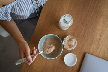 close up on female hands hold spoon with oat flakes and make breakfast