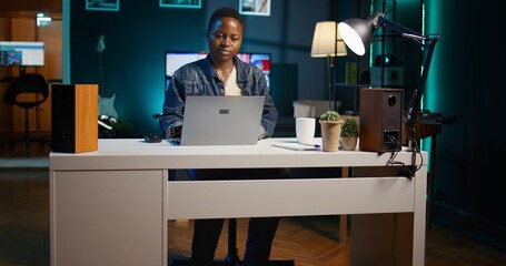 Freelancer in neon lit home office sitting at desk and typing on laptop keyboard. Remote employee...