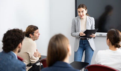 Positive skilled female coach explaining topic to group of people during foreign language class in...