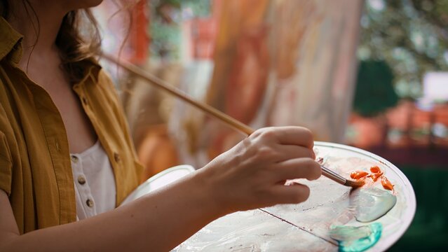 In an art studio, artist mixes a watercolor paints on a palette to create a rustic masterpiece on canvas. Woman painting with tools and showing her skill, artwork creation. Close up. Camera B.
