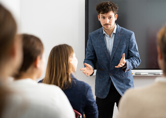 Positive skilled male coach explaining topic to group of people during foreign language class in...