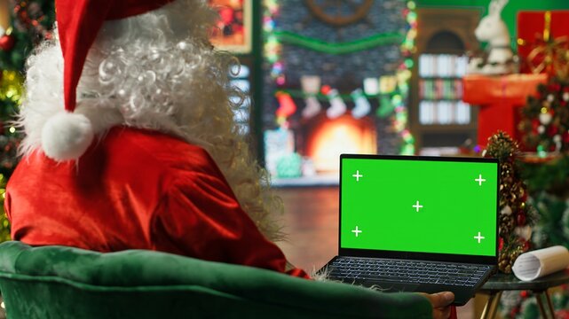 Santa Claus making list of kids who has been naughty or nice on green screen laptop. Person preparing travel plans on chroma key notebook before visiting children, camera A