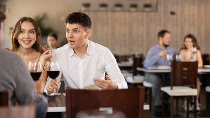 Three friends meeting in modern restaurant - men and a woman drinking wine, talking, discussing problems