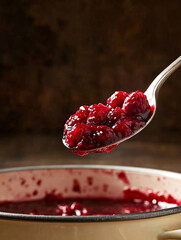 Raspberry jam on spoon above enamel pot in rustic kitchen