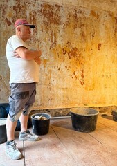  Experienced worker stands against a background of a torn wall in thought, making a plan