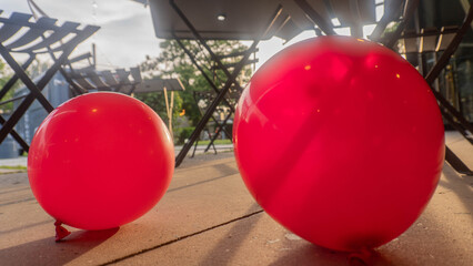 Two bright red balloons sit on the floor of a patio or terrace, illuminated by the warm evening...