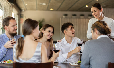 Young woman waitress taking order from group of friends at table in restaurant