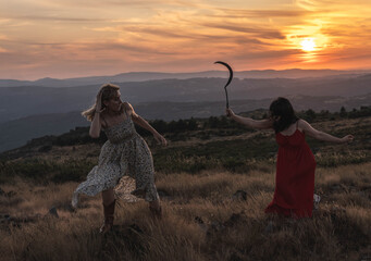 Dos mujeres en silueta se enfrentan en una colina durante un vibrante atardecer. Una de ellas, con...