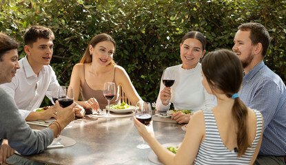 Group of men and women friends eating drinking and talking on restaurant terrace