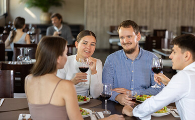 Two couples of young men and women drinking eating and talking in restaurant