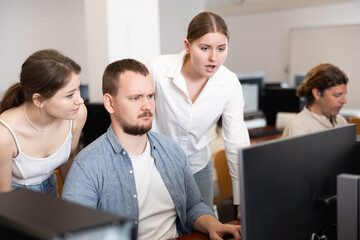Male teacher and students studying new program together on computer screen at university