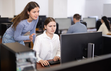 Female teacher of computer courses helps girl student to figure out with performance of difficult...