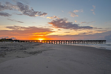 A vibrant orange/yellow sunrise, with beach and ocean in the foreground, and footprints in the sand...