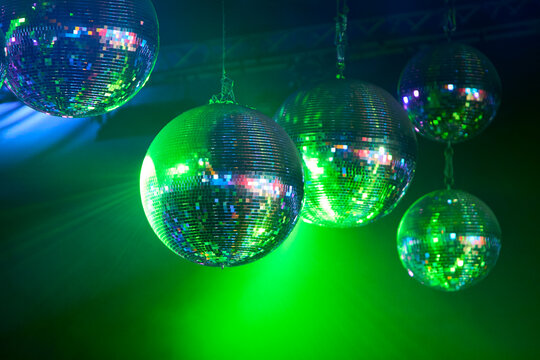 Imagen de 5 bolas disco colgantes que reflejan luces verdes y azules, evocando una atm&oacute;sfera de celebraci&oacute;n retro.