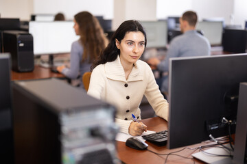 In group of students attending computer courses, female student looks at monitor screen and does...