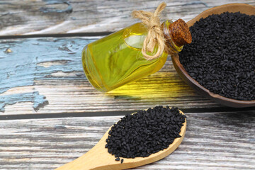 Black cumin seeds and essential oil with bowl and wooden shovel or spoon. Nigella Sativa in glass...