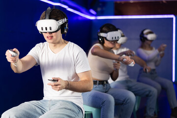 In dark hall of entertainment center, young guys and girls talking about spending time in virtual...