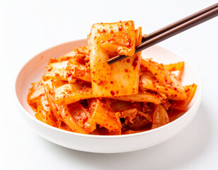 Spicy kimchi cabbage held by chopsticks over a white bowl, Korean cuisine