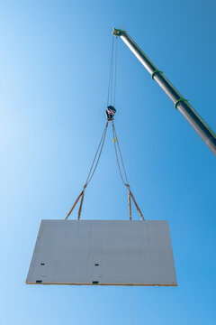 Prefabricated concrete wall being lifted by crane at construction site