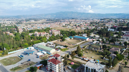 Fototapeta premium Aerial view of a densely populated town with buildings trees and distant mountains under a cloudy sky tanzania