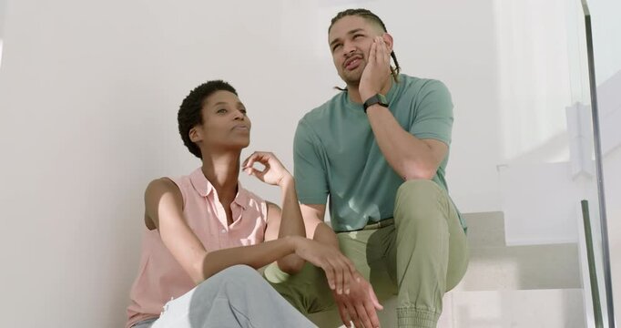 Couple conversing on white staircase wearing earbuds as woman initiating gestures to share ideas