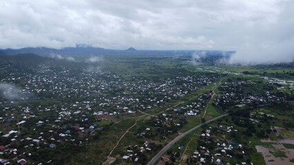 Aerial view of a densely populated town nestled among green hills under an overcast sky with low...