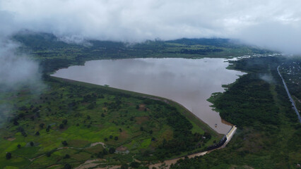 Aerial view of a lake surrounded by green vegetation and mountains under a cloudy sky landscape...