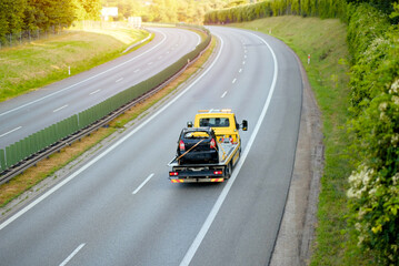 Yellow Tow Truck Transporting Burned Out Car on Empty Highway