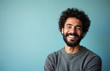 Obraz premium Close-up studio portrait of confident, smiling man with beard. He wears stylish grey sweater against blue background. His happy expression, fashionable appearance suggest modern, positive lifestyle.