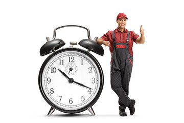 Full length portrait of a repairman with a tool box leaning on a big alarm clock and gesturing...