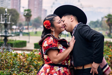 Portrait of a smiling young couple, dressed as Chilean huasos, posing romantically, about to kiss...