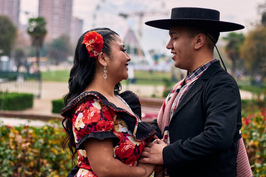 A young Chilean Latino couple dressed as Chilean huasos, very romantic and joyful, holding hands, about to kiss and dance the cueca, a traditional Chilean dance. Chilean Independence Day celebration.