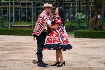 Portrait of a smiling young couple dressed as Chilean huasos, posing and joyfully dancing cueca...