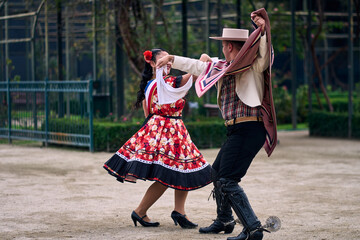 Portrait of a smiling young couple dressed as Chilean huasos, posing and joyfully dancing cueca...