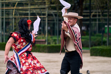 Portrait of a smiling young couple dressed as Chilean huasos, posing and joyfully dancing cueca...