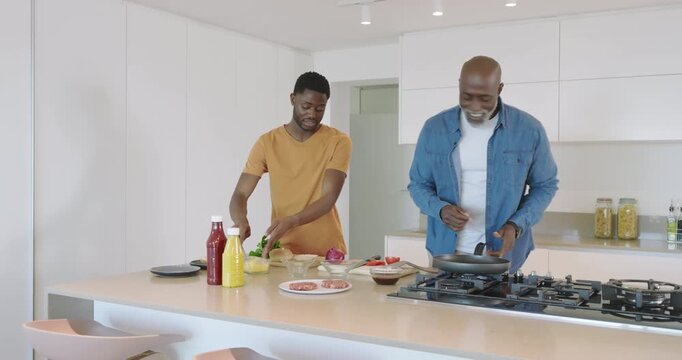 After slicing peppers African American father and son cooking at island flipping patties for dinner
