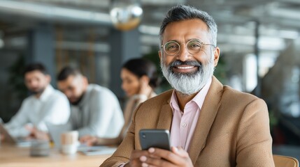 opy space are with smiling mature Latin or Indian businessman holding smartphone in office. Middle aged manager using cell phone mobile app. Digital technology application and solutions for business.