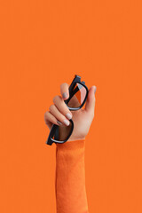 Womans hand holding 3d glasses on an orange background