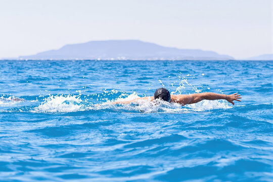 Man swimming butterfly stroke in open blue ocean water with a distant island, symbolizing fitness and freedom.