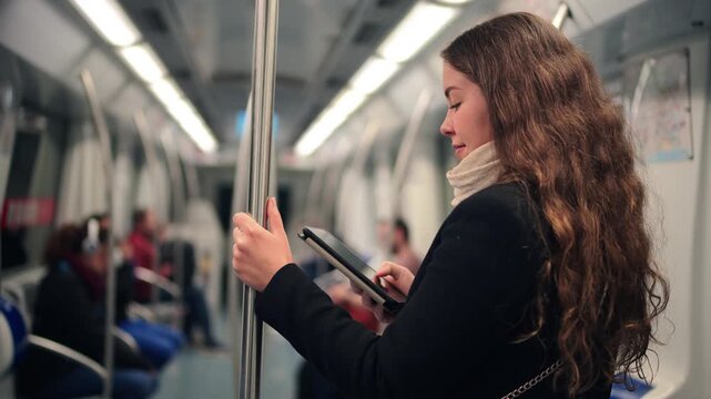 A young woman is actively reading an e-reader while riding on a subway train, showcasing her engagement with the digital content. Her focus and calm demeanor reflect a moment of personal enjoyment